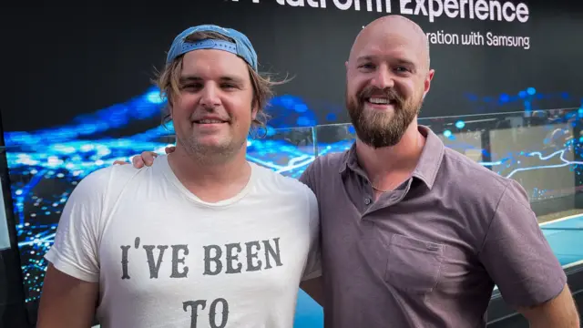 Two man stand facing the camera with their arms around each other